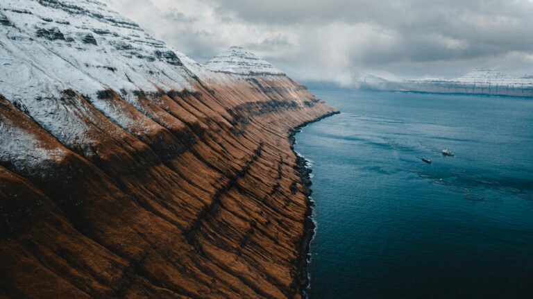 Dramatic aerial view of snow-capped mountains and ocean in the scenic Faroe Islands.