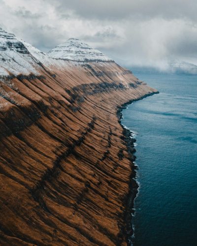 Dramatic aerial view of snow-capped mountains and ocean in the scenic Faroe Islands.